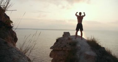 Genç adam sabah deniz kenarında büyük taş üzerinde güneş doğarken yapıyor