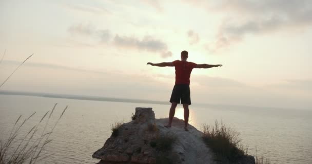 Junger Mann wärmt sich auf dem großen Stein am Meer auf — Stockvideo