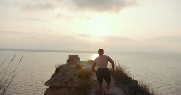 Giovane uomo in topless in piedi sul bordo di una scogliera godendo la natura — Video Stock