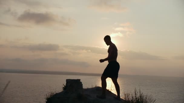 Mannelijke silhouet doet ochtend yoga op de grote steen door de zee bij zonsopgang — Stockvideo