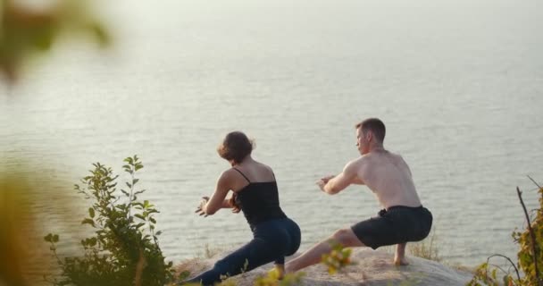 Pareja joven haciendo el calentamiento matutino en el acantilado junto al río — Vídeos de Stock