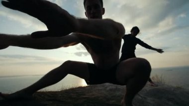 Genç adam ve kadın güneş doğarken sabah jimnastiği yapıyor