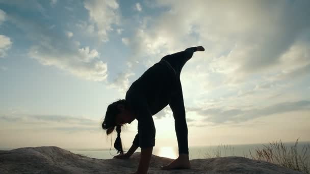 Жіночий силует практикує вправи балансу на скелі на сході сонця — стокове відео