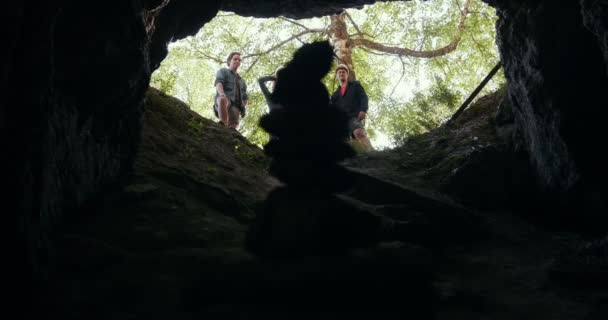 Jóvenes amigos excursionistas de pie a la entrada de la cueva en el bosque — Vídeo de stock