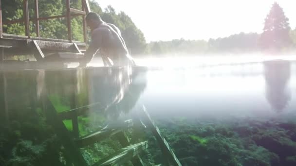 Muskulös man klättrar i trappan från den blå sjön — Stockvideo