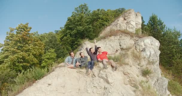 Jóvenes amigos sentados en el acantilado y haciendo selfie al aire libre — Vídeo de stock