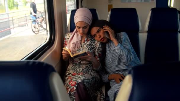 Deux femmes musulmanes voyageant en train, une femme lit, une autre parle au téléphone — Video