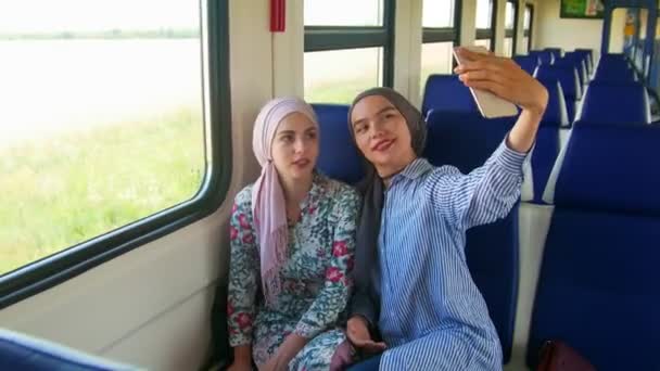 两个年轻的穆斯林妇女在头巾坐在座位上 乘坐火车 并采取自拍与电话 — 图库视频影像