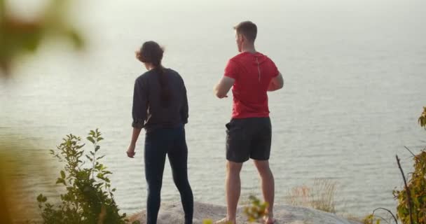 Jonge man en vrouw warming-up op de rots bij de rivier — Stockvideo