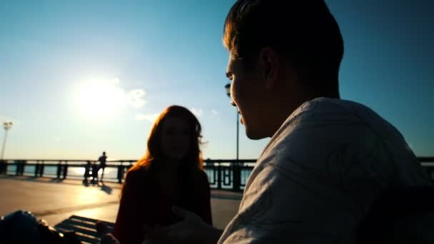 Jovem homem com deficiência conversando com uma jovem mulher na orla ao pôr do sol — Vídeo de Stock