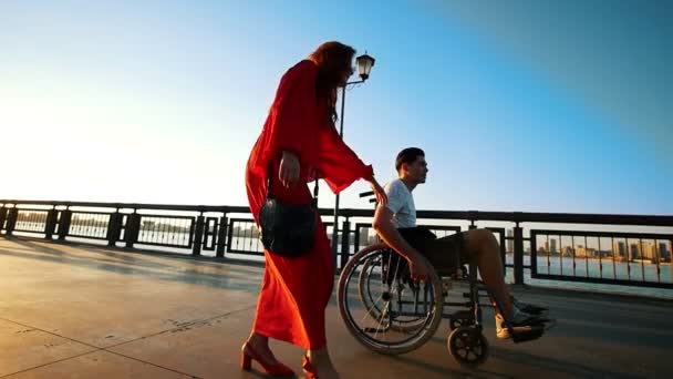 Joven hombre discapacitado en un paseo con una hermosa chica en el paseo marítimo en la noche de verano — Vídeos de Stock
