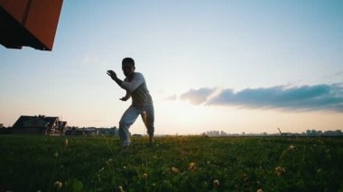 Güçlü atletik adam akrobasi gösterir ve capoeira günbatımı, yaz akşamları dans