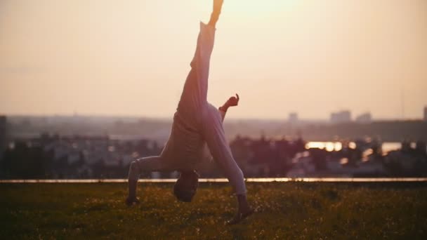 強い男は物理的にピンクの夕日の背景に芝生の上の非常にクールなトリックを示します — ストック動画