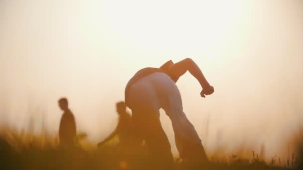 Starker Mann tanzt Capoeira vor dem Hintergrund vorbeifahrender Menschen bei Sonnenuntergang, Sommerabend — Stockvideo