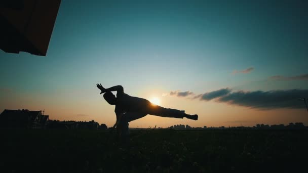Silhouette of a strong man dancing capoeira against the beautiful sky at sunset bronze color, summer evening — Stock Video