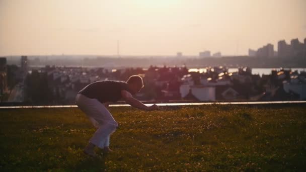 Hombre deportivo muestra la técnica de arte marcial de la capoeira en los rayos de una hermosa puesta de sol — Vídeos de Stock