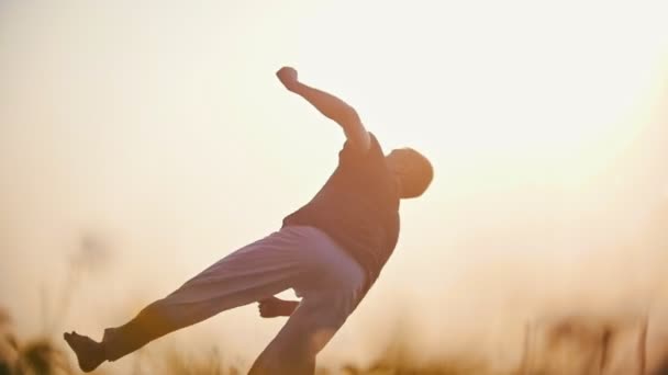 Homem atlético dançando capoeira, realiza um salto difícil no fundo de um belo pôr do sol de verão — Vídeo de Stock