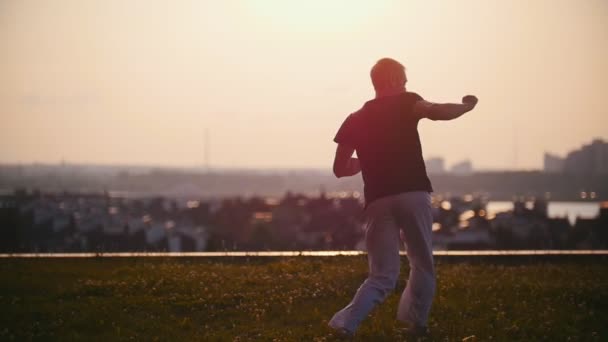Starker Mann führt Elemente der brasilianischen Kampfkunst Capoeira in den Strahlen des erstaunlichen Sommersonnenuntergangs vor — Stockvideo