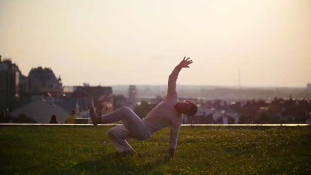 アスレチックの男が街の景色と美しい夕日の背景にカポエイラ ダンスのクールなトリックを示しています — ストック動画