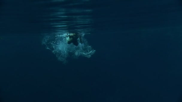 Атлетик плавает под водой, создает много пузырьков, вода синяя — стоковое видео