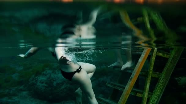 Girl with a tattoo in a swimsuit black swims under water, next to her man — Stock Video