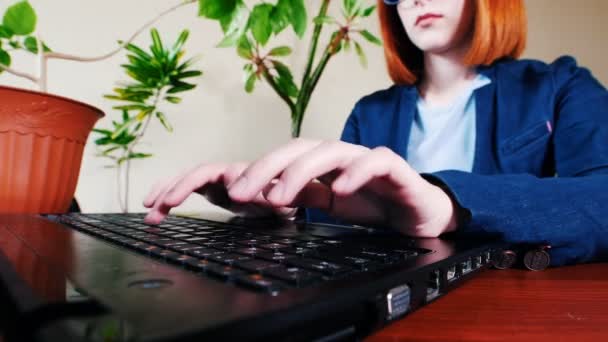 Young woman in eyeglasses typing the text on laptop in office