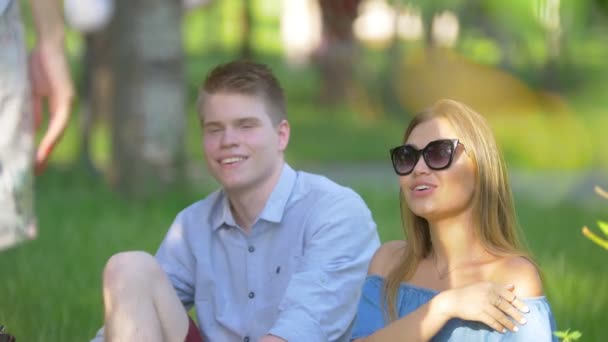 Des amis regardent les nuages assis sur l'herbe sous le soleil — Video