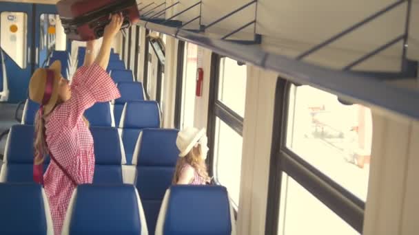 Joven madre atractiva con hija va a viajar en tren de velocidad - pone la maleta en el estante superior — Vídeo de stock