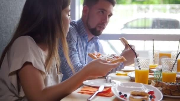 Quatre jeunes amis assis au café et mange le petit déjeuner - pizza, jus, desserts — Video