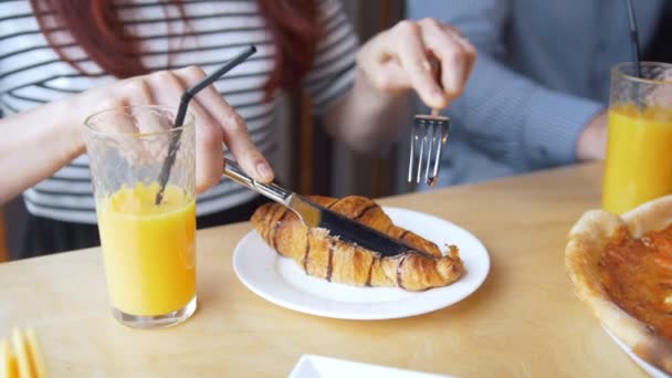 Jovem corta um saboroso croissant com uma faca e garfo comendo no restaurante — Vídeo de Stock