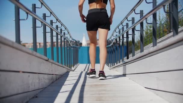 Menina esbelta em um terno de esportes preto está andando em uma plataforma de madeira branca — Vídeo de Stock