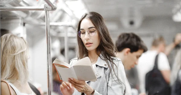 Menina lendo um livro no metrô no meio da multidão — Fotografia de Stock