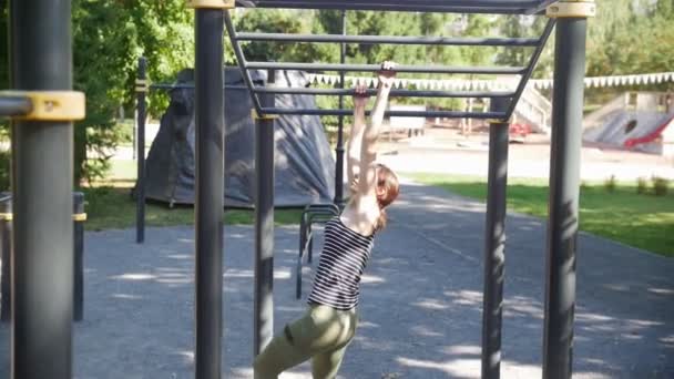 Молодые симпатичные делают упражнения и передвигаются на хонтальном баре в парке — стоковое видео