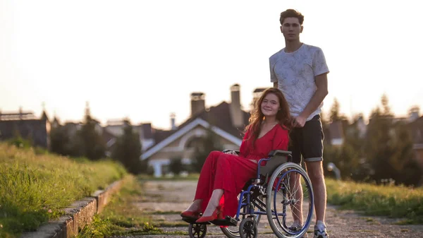 Fille en fauteuil roulant mignon parler à son jeune homme sur le fond de la maison, herbe verte — Photo