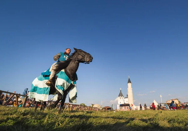 Βουλγαροκτόνος, Ρωσική Ομοσπονδία - Αυγούστου 2018, - ένας άνθρωπος σε μια πανοπλία Ιπποτών και ένα μπλε μανδύα σε ένα άλογο μπροστά από το τουρνουά για το φόντο της ιστορικής αρχιτεκτονικής δομής — Φωτογραφία Αρχείου