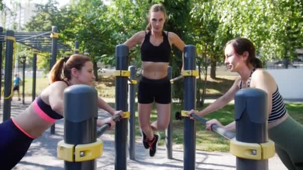 Tres chicas atractivas practican deportes en el parque en simuladores de hierro — Vídeos de Stock