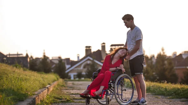 Fille en fauteuil roulant mignon parler à son jeune homme sur le fond de la maison, herbe verte et les arbres — Photo