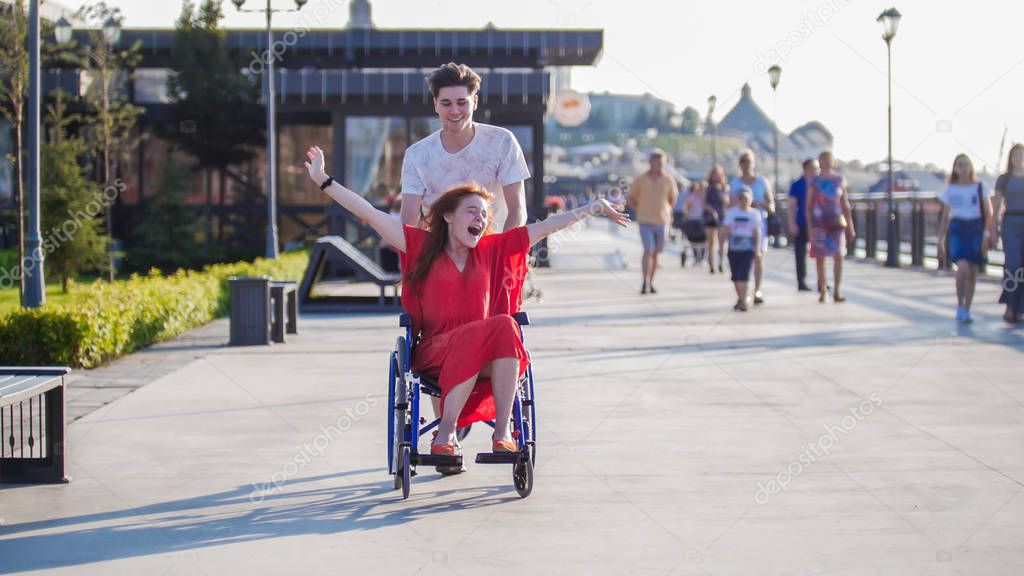 Guy rolls a happy disabled girl in a wheelchair on the waterfront