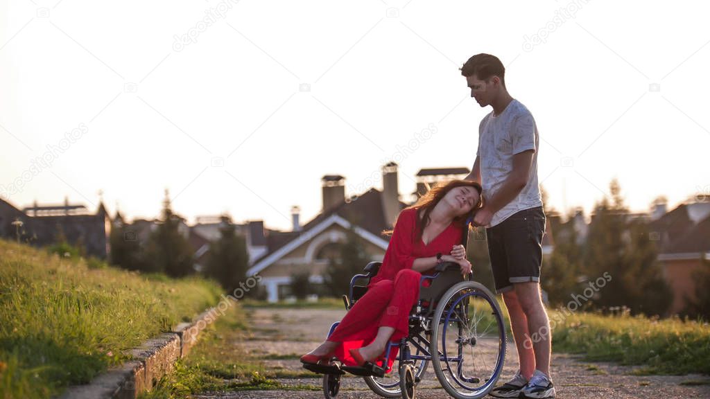 Girl in a wheelchair cute talking to her young man on the background of the house, green grass and trees