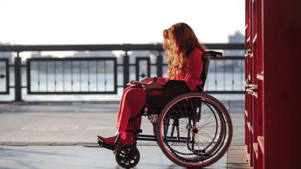 Молода руда дівчина читає книгу в інвалідному візку, на вулиці — стокове фото