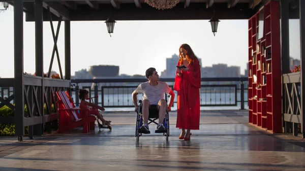 Bella giovane donna in passeggiata con un giovane in sedia a rotelle la sera d'estate — Foto Stock