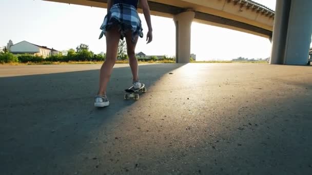 Маленькая стройная девочка катается на скейтборде под мостом и падает — стоковое видео