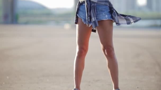 Vacker flicka i korta shorts, en t-shirt och en rutig skjorta på hennes bälte innehar en skridsko och ser på kameran — Stockvideo