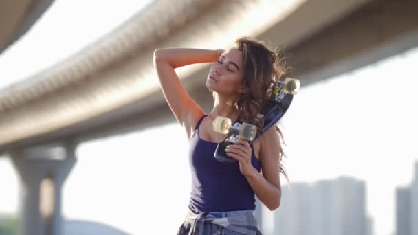 Fille tient une main de patinage pressée contre son épaule, l'autre main redresse ses cheveux, le vent souffle — Video