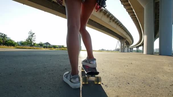 Jong meisje met slanke benen rijden op een skateboard onder de brug — Stockvideo