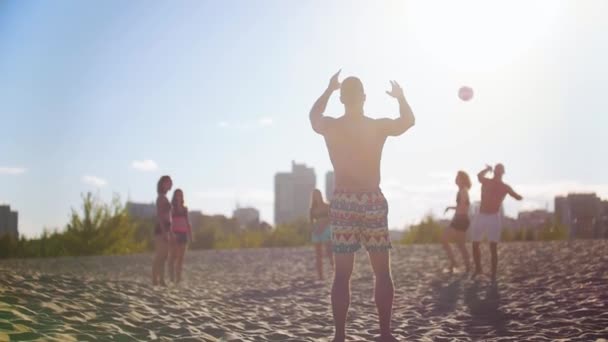 Компания молодых людей, играющих в пляжный волейбол, спортсмен забирает мяч у другого мужчины — стоковое видео