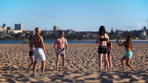 运动的年轻漂亮的人在河边的沙滩上打排球 — 图库视频影像