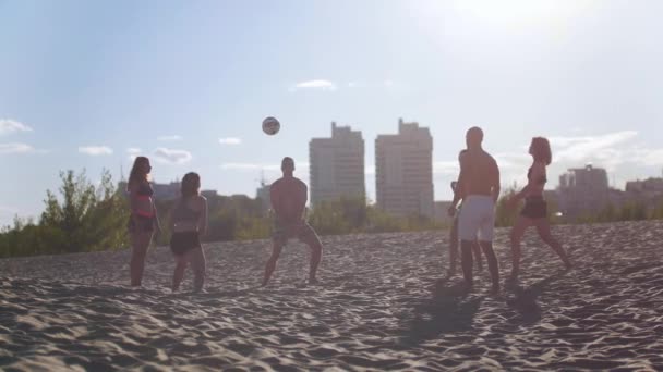 Красивые юноши и девушки играют в волейбол на песке под мягким вечерним солнцем — стоковое видео