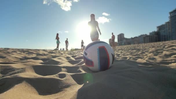 En primer plano está la pelota, una joven esbelta corre hacia arriba, la recoge y corre con la pelota en sus manos al resto de los jugadores en voleibol playa — Vídeos de Stock