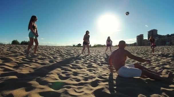 La compañía de jóvenes deportistas que juegan voleibol playa, uno de los jugadores se levanta de la arena después de la caída — Vídeo de stock